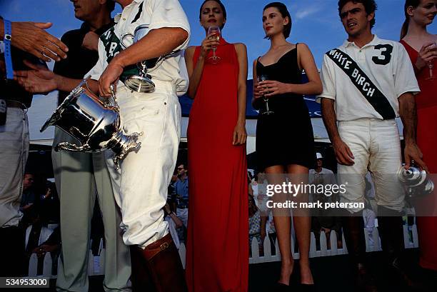 Wealthy people attending the Bridgehampton Polo Club's Mercedes Benz Polo Challenge. The winners of the tournament hold silver trophy cups while...