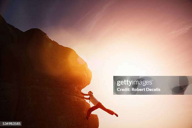 female free climber holding onto rock face - freiklettern stock-fotos und bilder