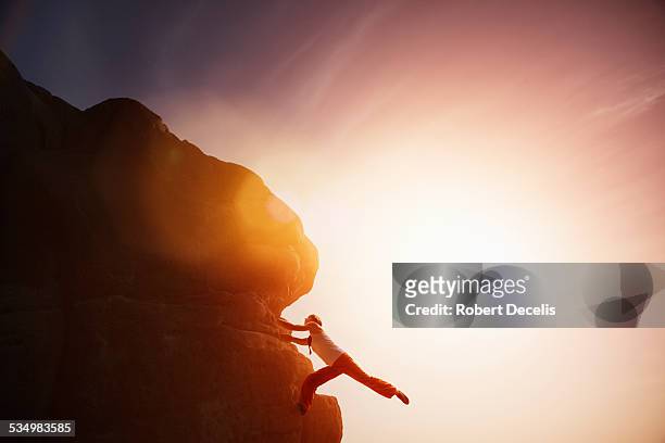 female free climber holding onto rock face - escalada libre fotografías e imágenes de stock
