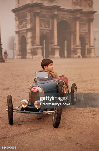 Young boy sits behind the wheel of a child's miniature car that was originally designed by Ettore Bugatti near the Arc de Triomphe du Carrousel in...