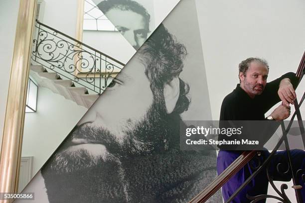 Fashion designer Gianni Versace poses on the stairs in his home in 1990, next to a photo montage of himself.