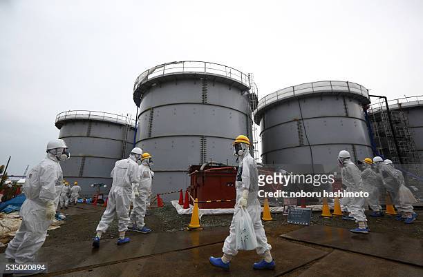 Members of the media and Tokyo Electric Power Co. Employees wearing protective suits and masks walk past storage tanks for radioactive water in the...