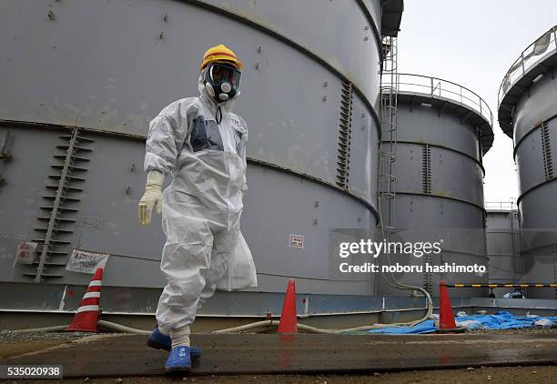 Tokyo Electric Power Co. Employee wearing a protective suit and a mask walks past storage tanks for radioactive water in the H4 area at the Fukushima...