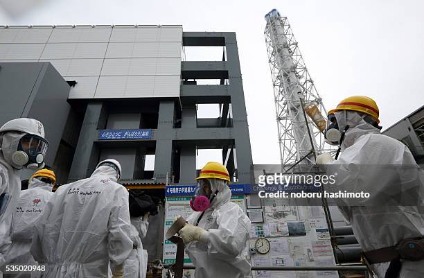 Members of the media and Tokyo Electric Power Co. Employees wearing protective suits and masks stand in front of the no. 4 reactor building at the...