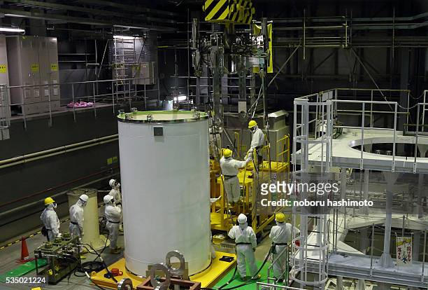 Workers wearing protective suits and masks work on a crane for a transport container inside the building housing the No. 4 reactor at Tokyo Electric...