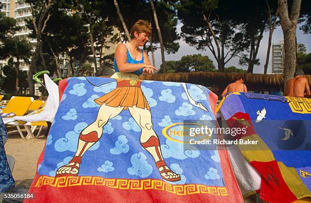 British lady applies a layer of sun cream to her hand on a beach in Magaluf. In the foreground, and aligned with the lady's own body is a sun lounger...