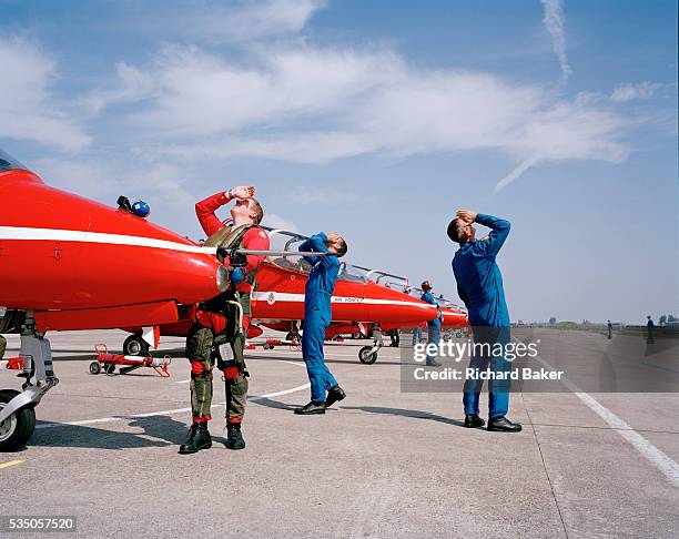 Craning their necks skyward, both a pilot and support ground engineers of elite 'Red Arrows', Britain's prestigious Royal Air Force aerobatic team,...