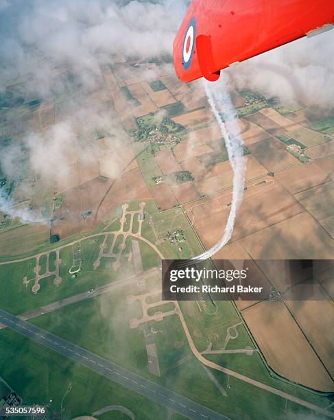 With the runways and former nuclear silos of RAF Scampton below, Lincolnshire, the elite 'Red Arrows', Britain's prestigious Royal Air Force...