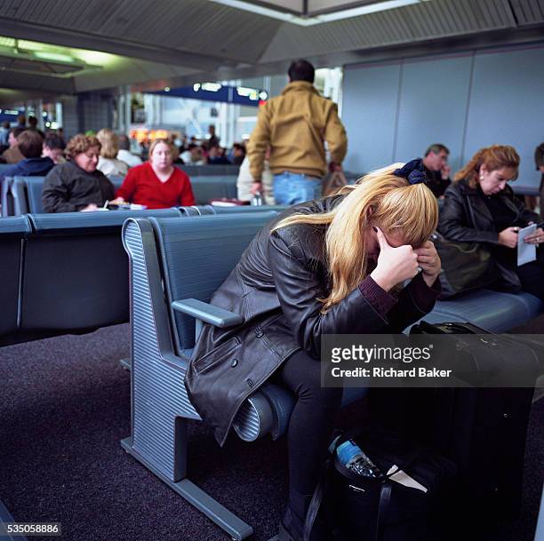 Female passenger leans forward with head in hands amid the busy terminal at Chicago O'Hare Airport, Illinois, USA. Fellow-travellers in the...