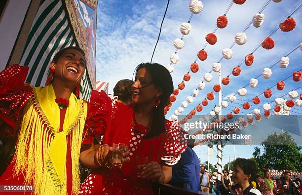 Two ladies parade down an avenue during the Spring Feria in Seville, Spain. Beneath dozens of colourful decorations which hang from cables above...