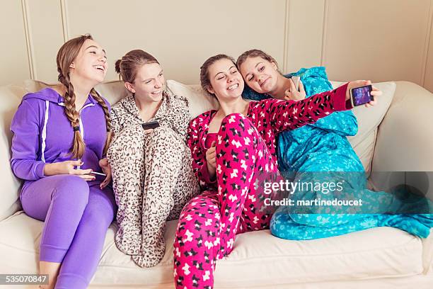 girlfriends wearing onesies chilling on a couch with mobile phones. - babygro stock pictures, royalty-free photos & images