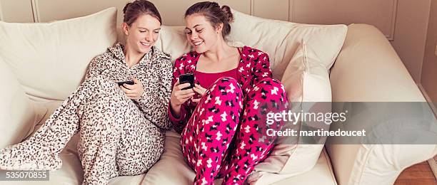 girlfriends wearing onesies chilling on a couch with mobile phones. - sparkdräkt bildbanksfoton och bilder