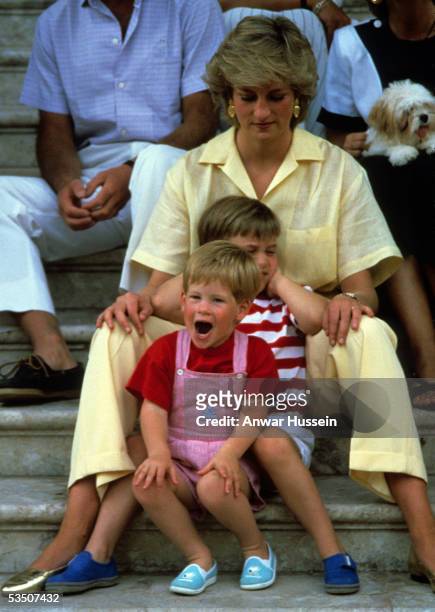 Diana, Princess of Wales, wearing a yellow jumpsuit, Prince William and Prince Harry sit on the steps of Marivent Palace with members of the Spanish...