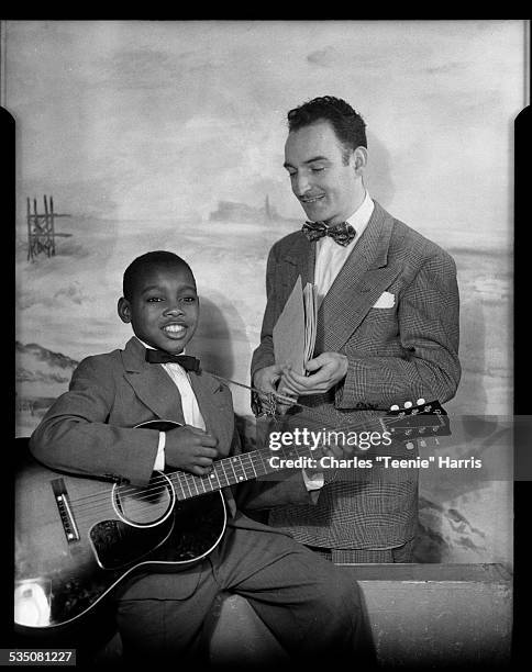 Young George Benson holding guitar, seated next to his manager Harry Tepper, in front of seascape background, Harris Studio, Pittsburgh,...