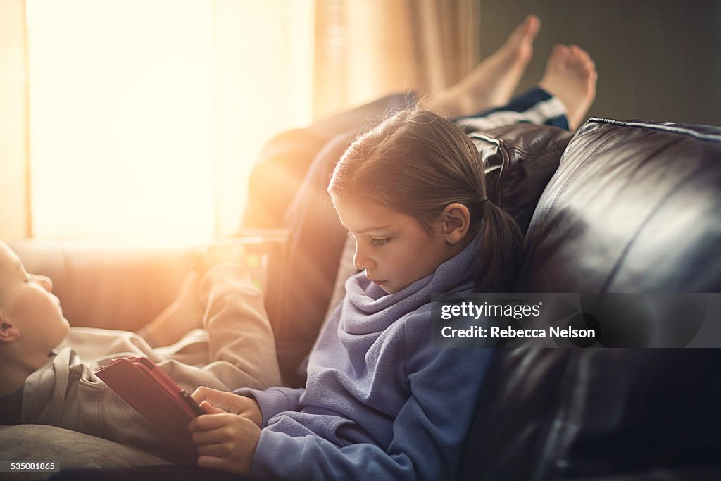 Boy and girl lounging on couch using tablets