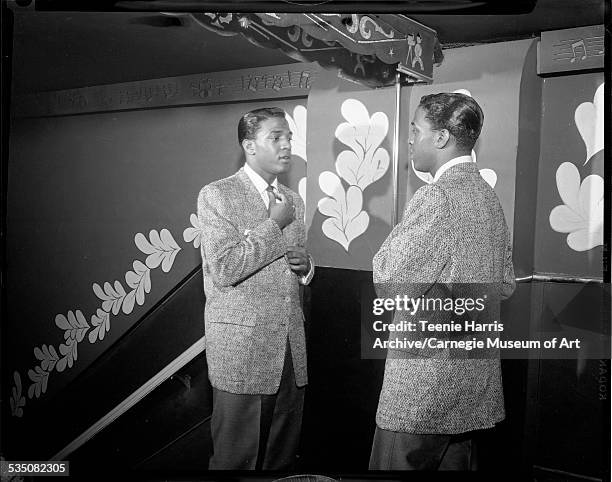 Clyde McPhatter standing in front of mirror adjusting tie, with musical notes and leaves patterned border on wall, in reflected in mirror,...