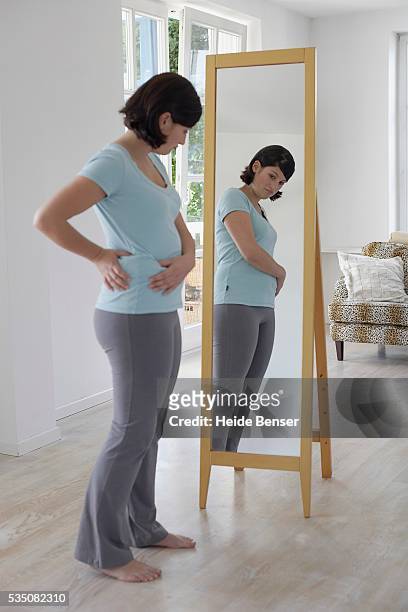 woman looking at her body in the mirror - full length mirror stock-fotos und bilder