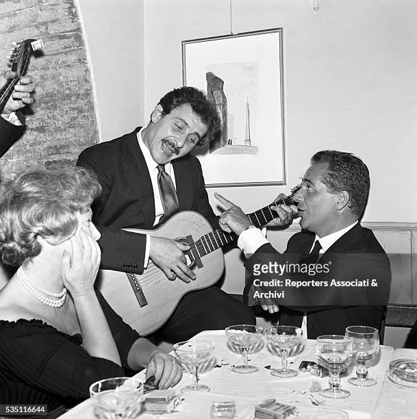Italian actor Rossano Brazzi singing accompanied by Italian singer-songwriter Domenico Modugno at the guitar during a dinner at the restaurant...