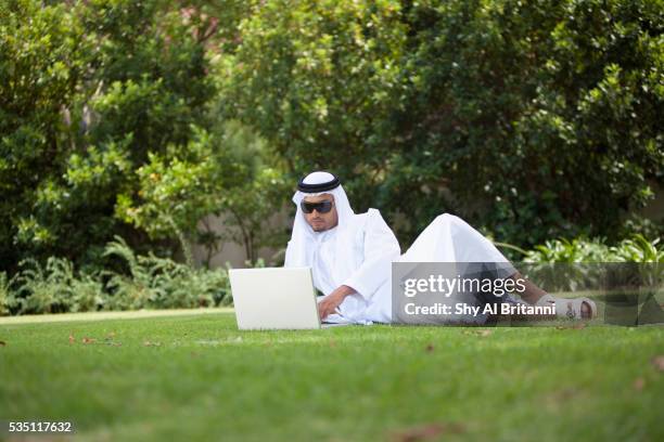 arab man using laptop in park. - emirati laptop stock pictures, royalty-free photos & images