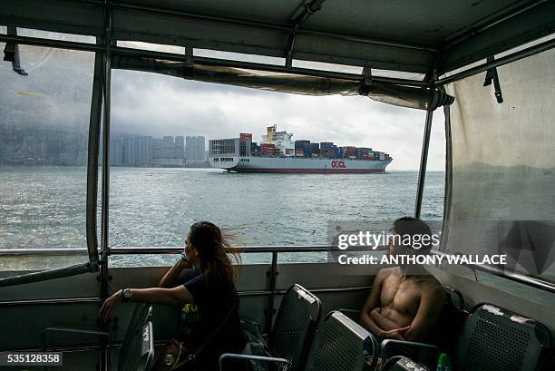 Ferry passengers look on as a cargo ship sails past during their commute between Lamma island and Hong Kong island early on May 29, 2016. / AFP /...