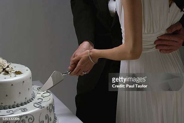groom holding bride close, cutting wedding cake - ent stockfoto's en -beelden