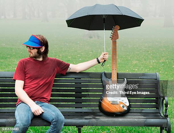 man holding umbrella over electric guitar - physical position photos et images de collection