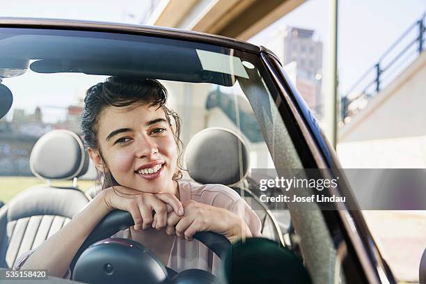 portrait of woman leaning on steering wheel - josef lindau stock-fotos und bilder