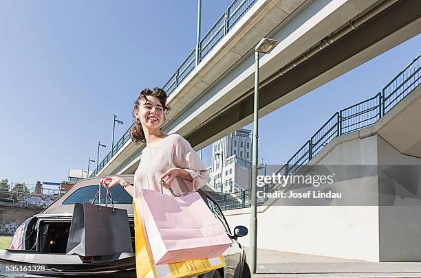 smiling woman carrying shopping bags to her car - josef lindau stock-fotos und bilder