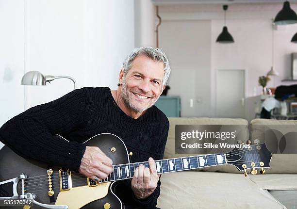portrait of man sitting at home and playing guitar - photograph 51 play stockfoto's en -beelden
