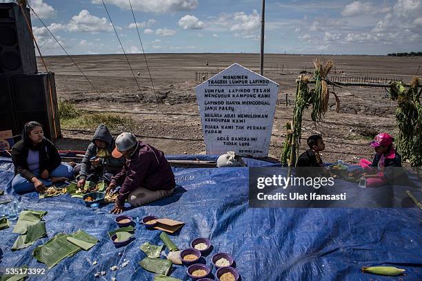 Residents of villages eat after pray together at mudflow during the tenth anniversary of the mudflow eruption on May 29, 2016 in Sidoarjo, East Java,...