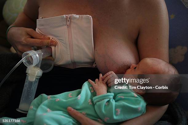 Two month old baby girl baby breast feeding as her mother uses a milk pump to express milk into a container on her other breast. Photo Tim Clayton