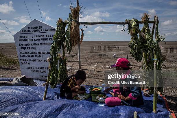 Two children eat after they pray together at mudflow during the tenth anniversary of the mudflow eruption on May 29, 2016 in Sidoarjo, East Java,...