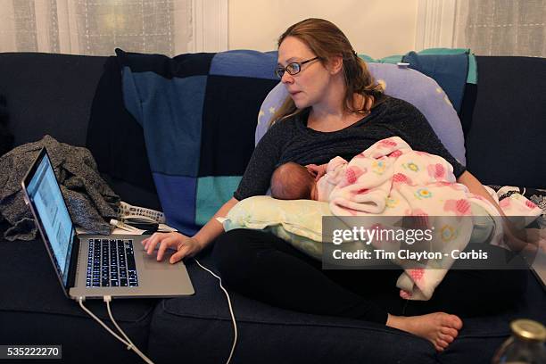 Mother breast feeds her new born baby girl while working on computers at home. Photo Tim Clayton