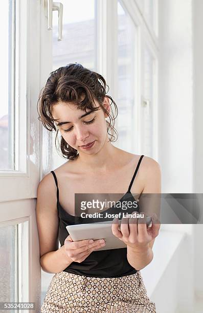 woman by window reading tablet computer - josef lindau stock-fotos und bilder