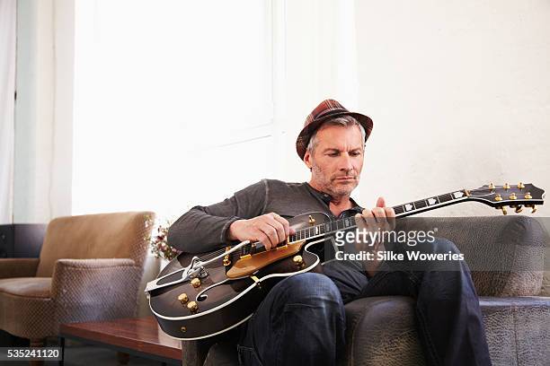 portrait of man in hat sitting at home and playing guitar - man playing guitar photos et images de collection