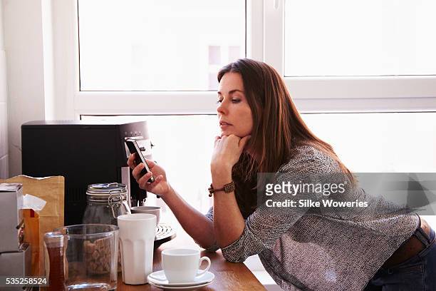 middle-aged woman texting on her smartphone - kaffeemaschine stock-fotos und bilder