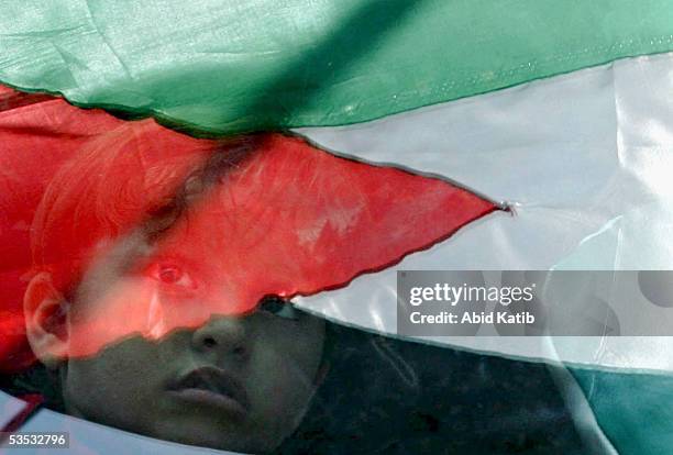 Palestinian national flag is reflected in a bus window while a child looks out at women celebrating the Israeli withdrawal from Gaza in front of the...