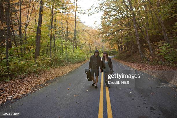 young couple walking hand in hand down a road - guitar case fotografías e imágenes de stock