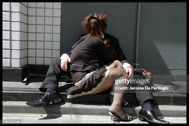 Young couple tries to recuperate on the sidewalk after a long night out without sleep.