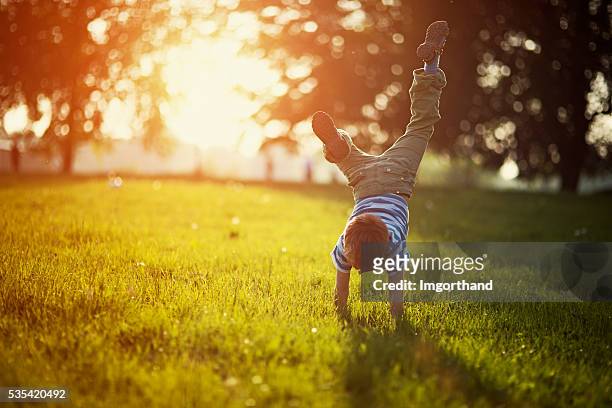 piccolo ragazzo in piedi sulle mani sull'erba - fare la verticale sulle mani foto e immagini stock