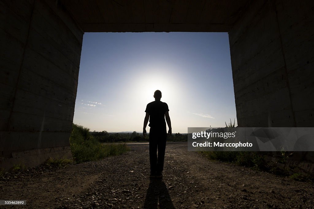 Man standing at large passage of concrete building, blocking sunlight