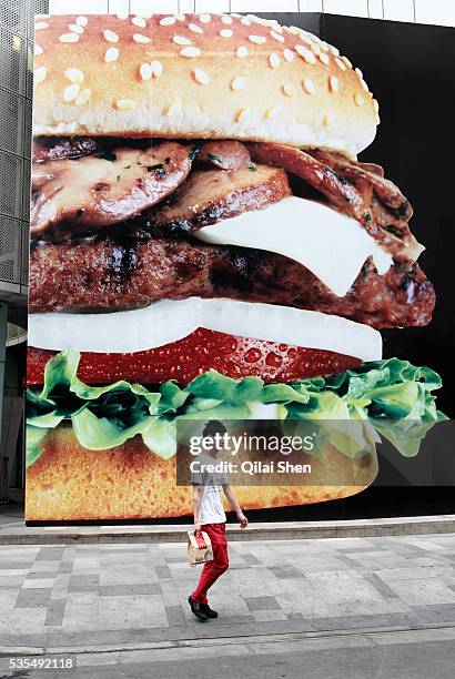 Man carrying a McDonald's takeout bag walks past a large hamburger advertisement in Shanghai, China on 20 May 2010.