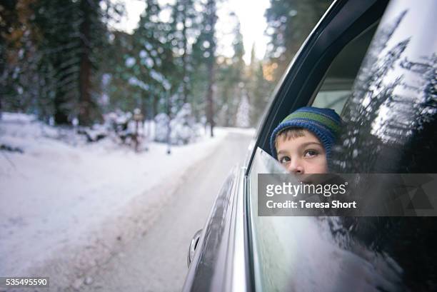 child looking out open car window while driving through snow - winter car window stock-fotos und bilder