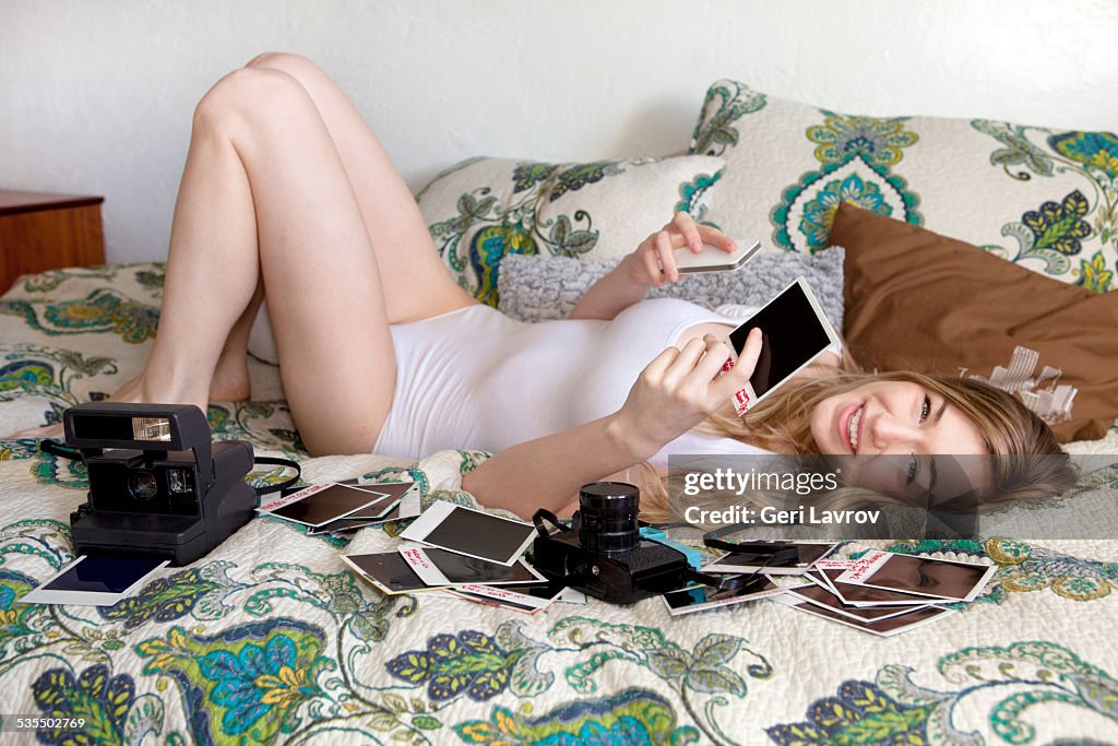 Young woman lying in bed looking at photo prints