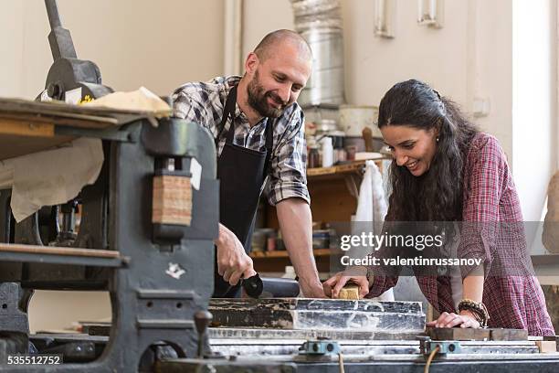 couple lithography workers using printing press at workshop - lithography printing stock pictures, royalty-free photos & images