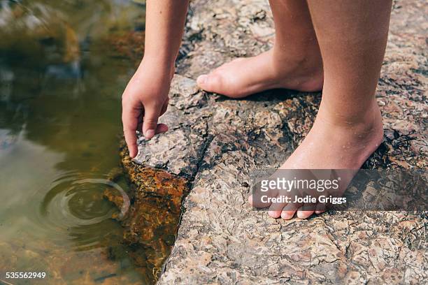 child with bare feet leaning down to touch water - bare kids foto e immagini stock