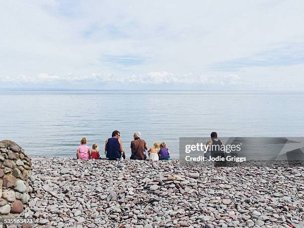 family sitting on rocky beach looking at ocean - porlock weir stockfoto's en -beelden