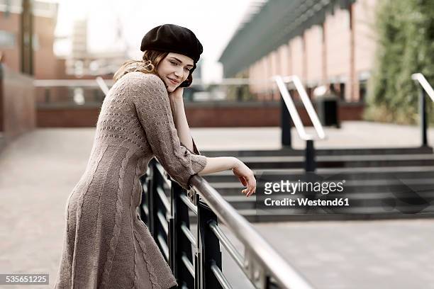 portrait of young woman wearing beret and knitted dress leaning on a railing - vestito di maglia foto e immagini stock