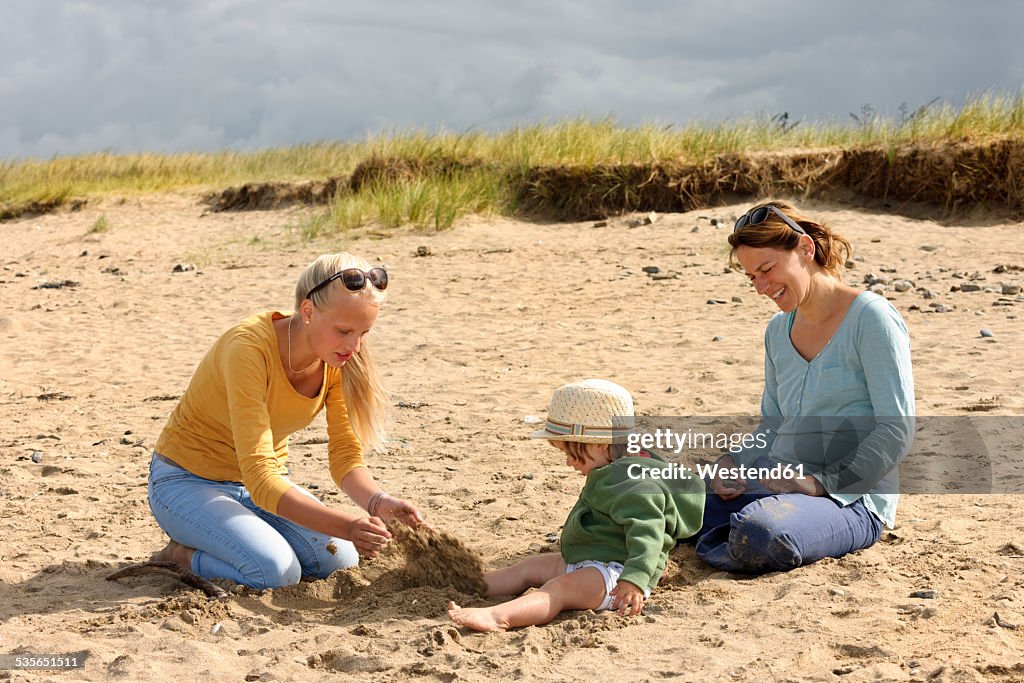 France, Britanny, Sainte-Anne-la-Palud, mother and her two daughters sitting on beach dune