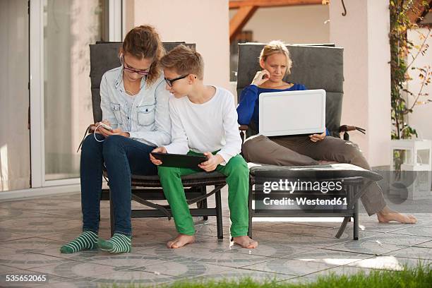 mother and her two children relaxing with digital tablet, smartphone and laptop on the terrace - 3 teenagers mobile outdoors stock-fotos und bilder